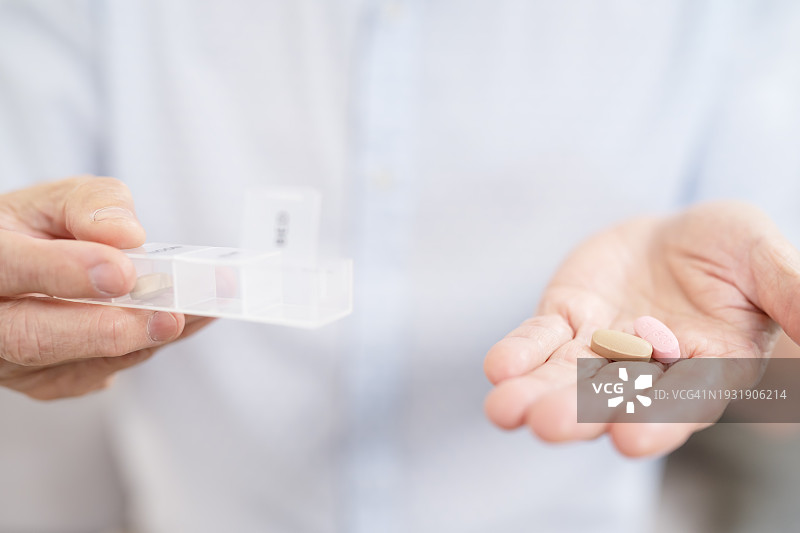 老年人使用药物整理盒和药物提醒器轻松区分。一位老年男性拿着药丸或维生素和药盒服用每日剂量图片素材