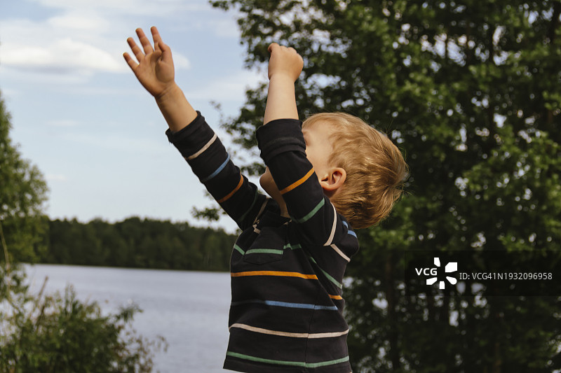 在远离城市的湖泊和森林附近，夏季乡村里跳跃玩耍的男孩肖像。私密和安静。防虫剂图片素材