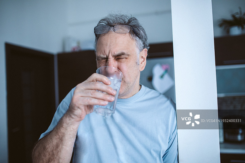 冰镇的苦楚：一位中年男人因牙齿剧痛而畏缩，喝着冰水，暴露了牙本质过敏的影响。头痛图片素材