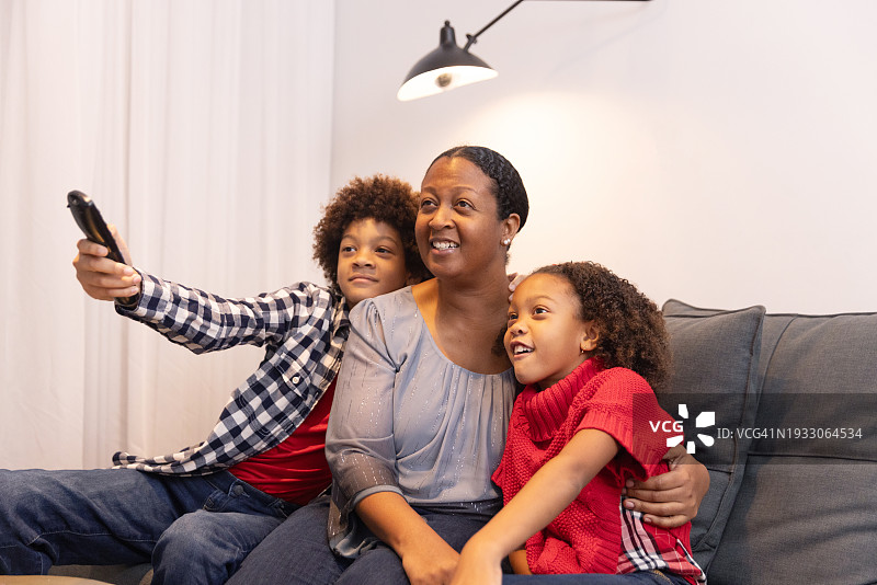 一位非裔美国母亲和她的两个混血孩子坐在沙发上看电视，身穿休闲装图片素材