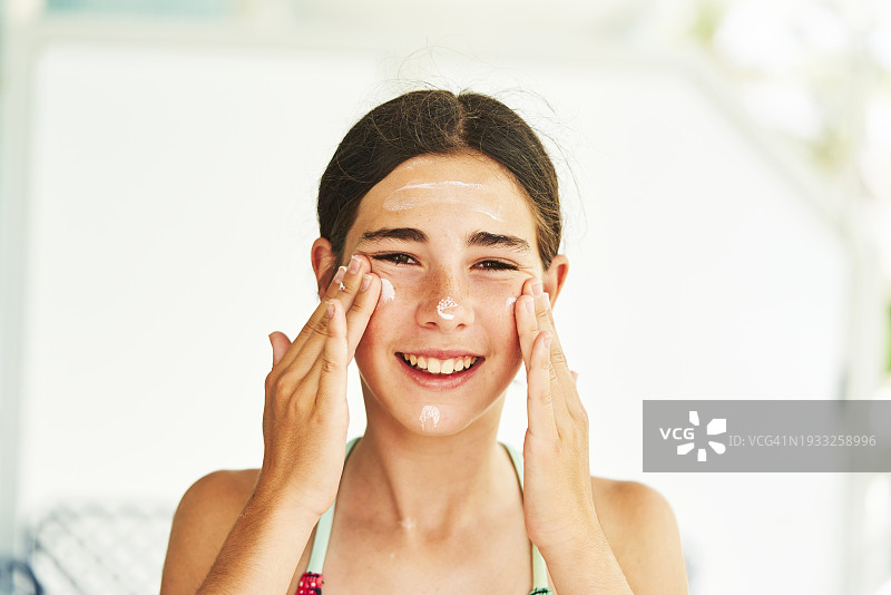 一位美丽的年轻女人在脸颊上涂抹面霜，面带微笑地看着镜头，正面视角图片素材