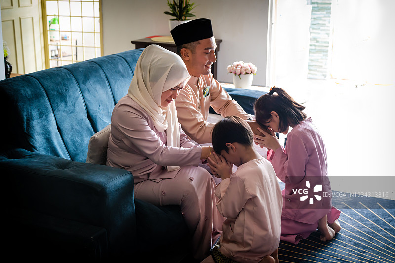 在开斋节庆祝活动期间，穿着传统服装的马来穆斯林小男孩和女孩向父母道歉图片素材