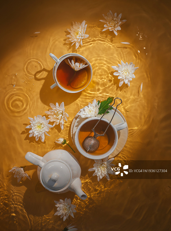 阳光明媚的下午茶场景：阳光下浸没在金色茶水中的杯子和甘菊花图片素材