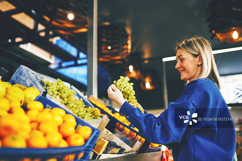 年轻女人在市场购买水果，挑选葡萄图片素材