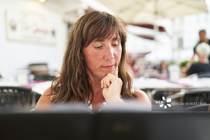 美丽的女人坐在餐厅里看菜单，面露沉思，前景视角图片素材
