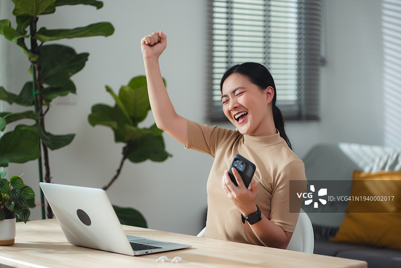 亚洲女性在家办公，使用智能手机做出胜利的手势图片素材