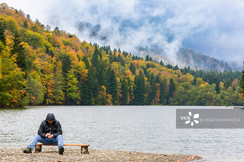 男人在秋天坐在湖边的长椅上图片素材