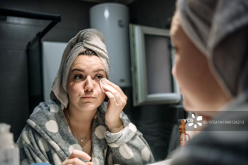 年轻女子在浴室进行个人护理，早上进行卫生清洁，在脸上涂抹乳霜图片素材