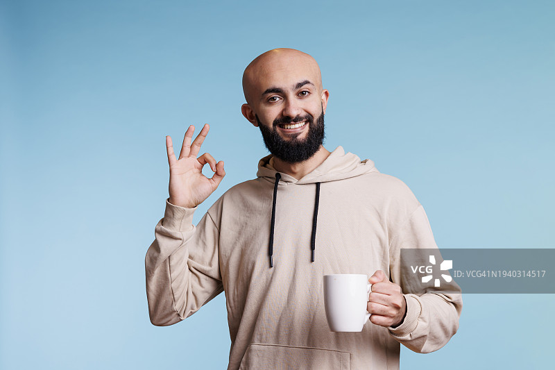 微笑的男人在蓝色背景前做手势的肖像图片素材