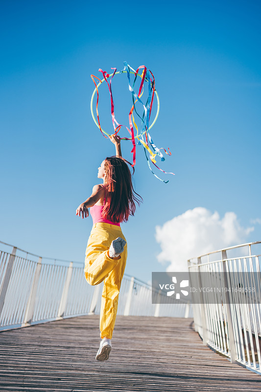 快乐的年轻女子在蓝天下舞动彩色丝带图片素材