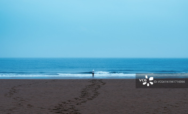 在远处，一个年轻男人在雨天面向大海图片素材