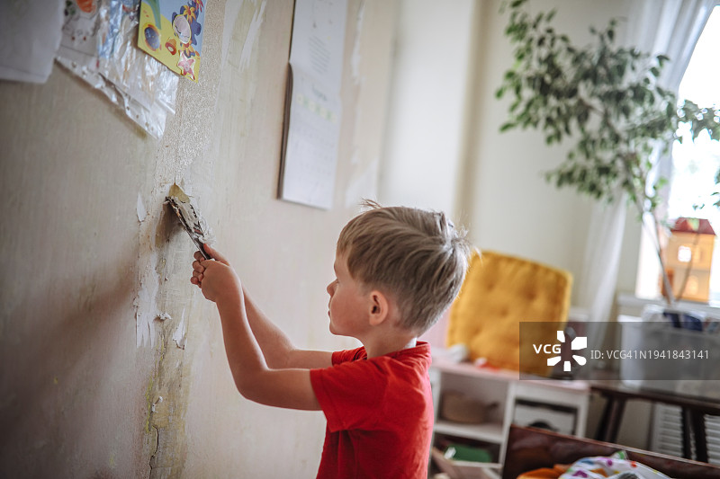 家庭乐趣：年轻装修工移除壁纸，小帮手在行动图片素材