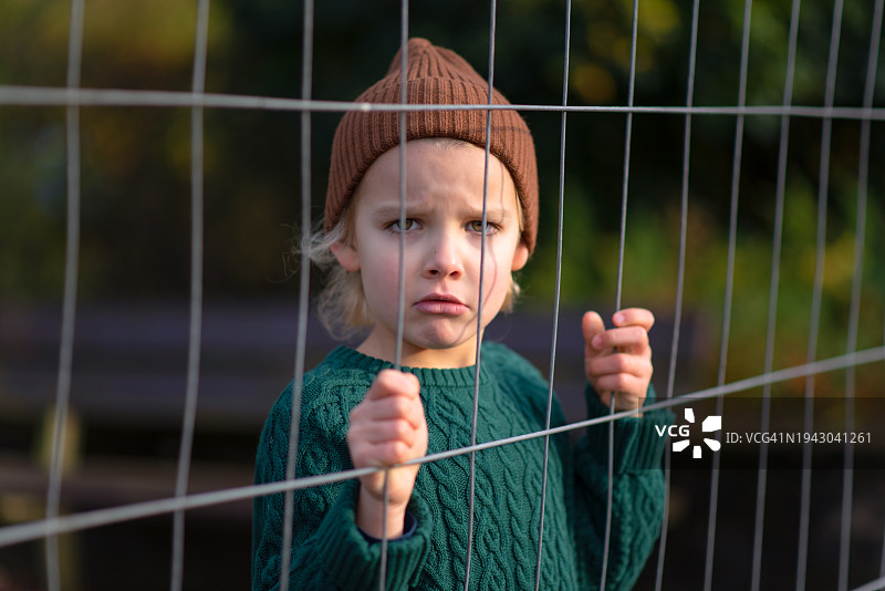 一个男孩悲伤地站在栅栏后面图片素材