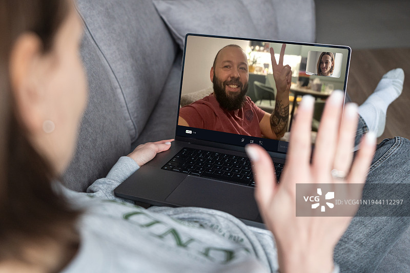 在线约会和在线交流。年轻女子躺在沙发上，用笔记本电脑与朋友、男友或丈夫进行视频通话。图片素材