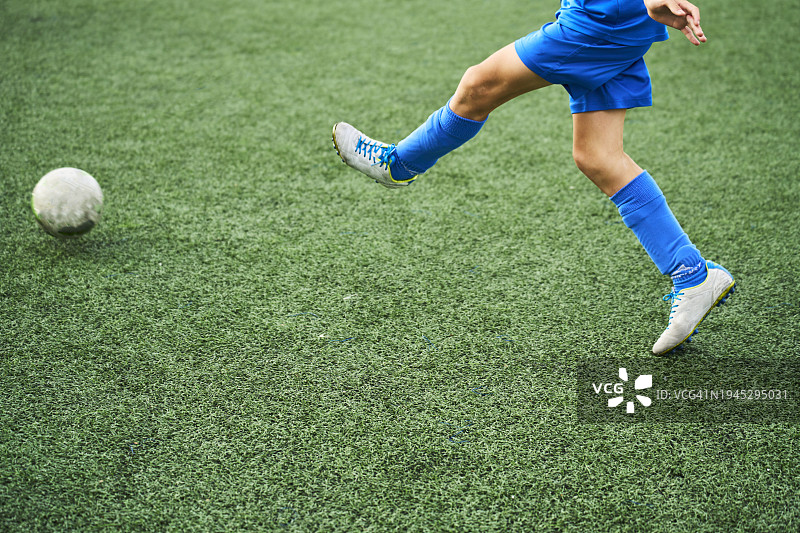 穿着运动服的男孩在足球场上比赛踢球的腿部特写，正面视角图片素材