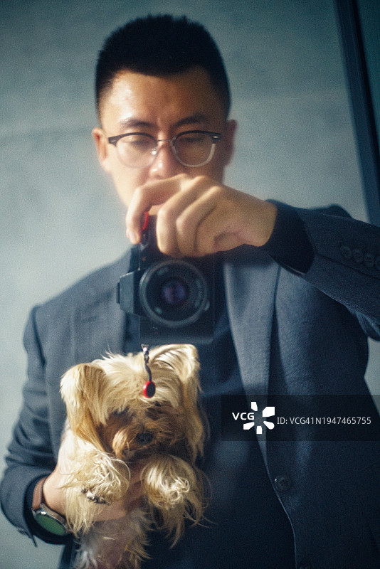 穿着西装的年轻男子抱着宠物狗自拍图片素材
