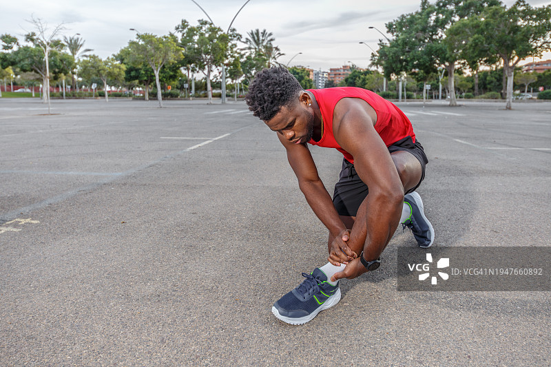 男运动员在停车场扭伤脚踝，蹲下身子，露出痛苦的表情图片素材