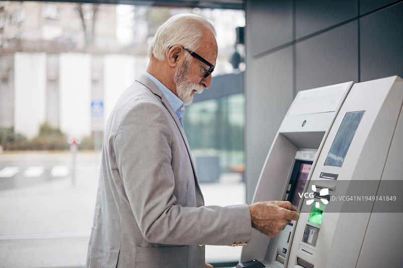 一位老人在火车站用借记卡从ATM取款图片素材