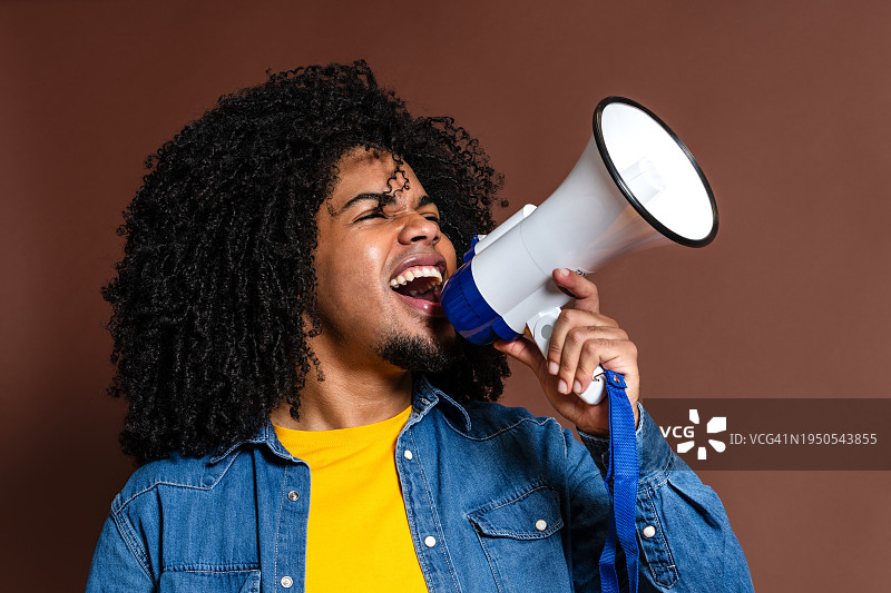 充满魅力的非裔拉丁裔男子对着扩音器喊叫，并在工作室里竖起大拇指图片素材