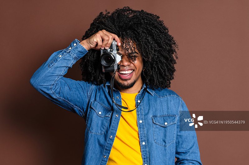 在棕色制服背景上手持老式相机的快乐非洲裔拉丁摄影师图片素材