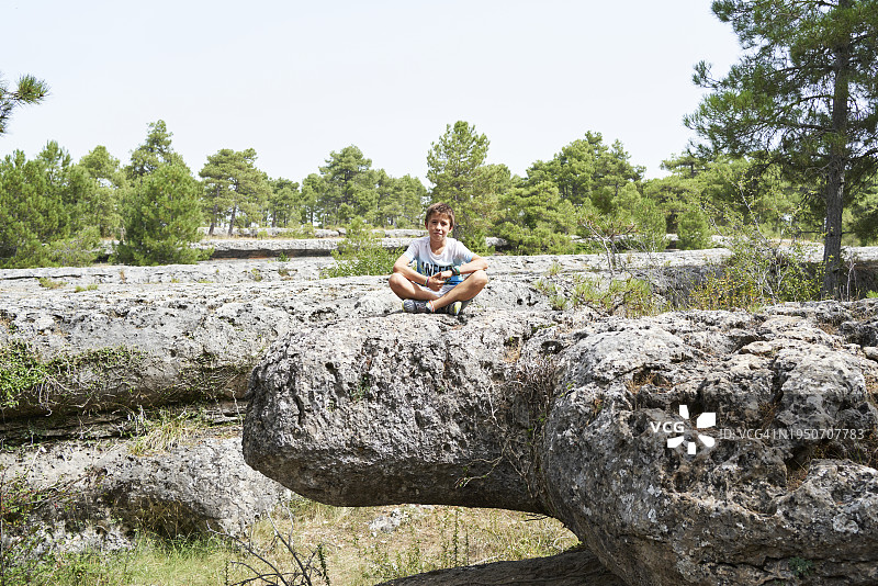在昆卡古城岩石上微笑看着镜头的游客男孩肖像，正面视角图片素材