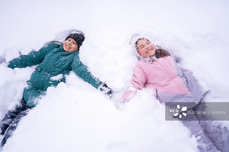 兄妹俩带着调皮的笑容躺在蓬松的白雪中手牵着手图片素材