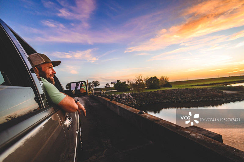 男子在公路旅行中，靠在车窗边欣赏美丽的日落图片素材