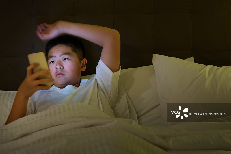 在床上使用手机的青少年男孩图片素材