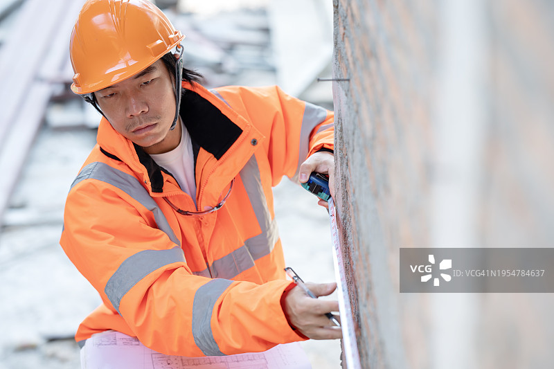 建筑质量保证检验，确保项目质量。建筑工头在施工阶段用卷尺测量建筑墙壁，以符合标准。图片素材