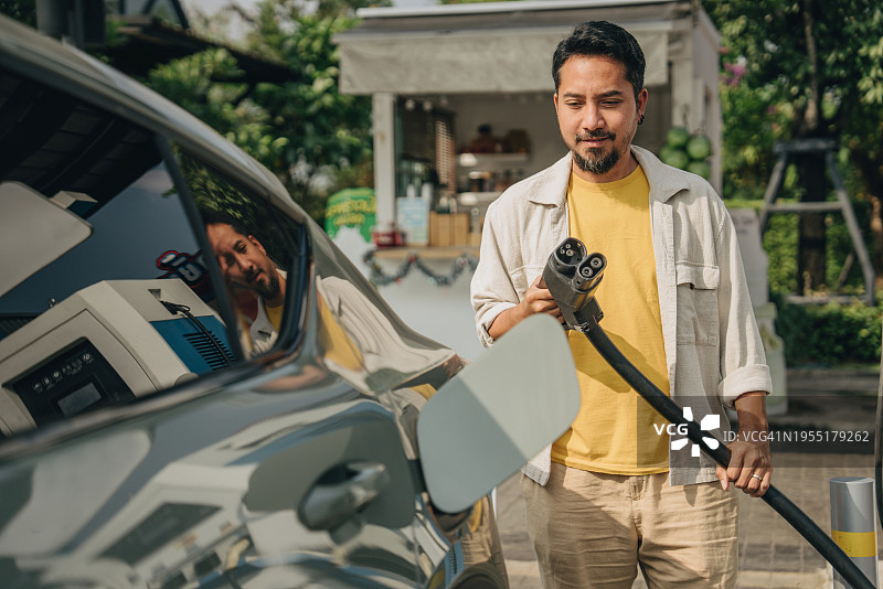 在泰国曼谷，亚洲男人正在打开汽车引擎盖为电动汽车加油图片素材