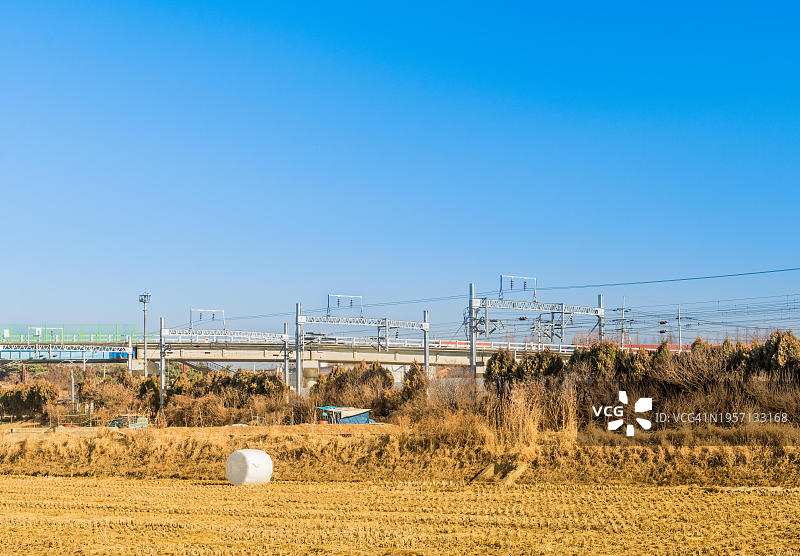 韩国亚洲，高速公路立交桥旁的铁路轨道前方的收割田地景观，有金属输电塔图片素材