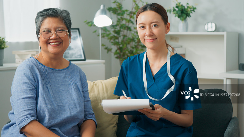 亚裔女医生为老年女患者进行健康检查，两人舒适地坐在沙发上微笑图片素材