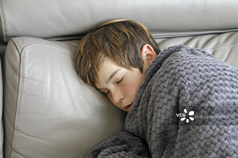 感冒男孩裹着毯子坐在沙发上图片素材