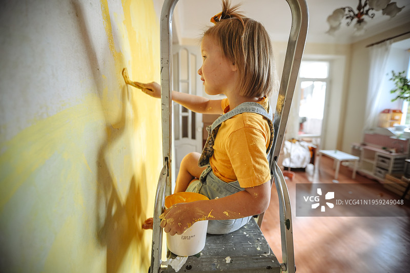 在家装期间粉刷黄色墙壁的快乐女孩图片素材