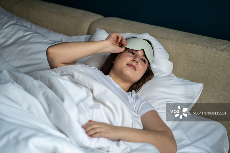 在床上醒来摘下睡眠眼罩的年轻女人图片素材