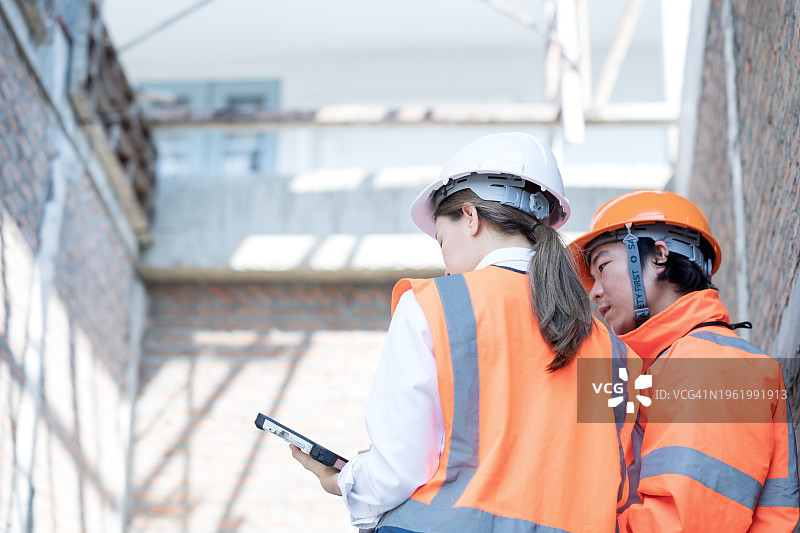 利用施工项目管理提高效率和生产力。 一名女性项目经理和一名男性建筑工程师在建筑工地上，一边讨论项目计划，一边查看平板电脑上的进度。图片素材