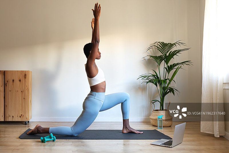 年轻的非裔美国女子在家用笔记本电脑练习瑜伽图片素材