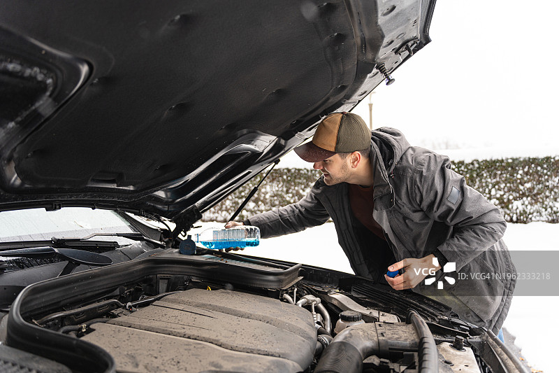 冬天寒冷天气里往汽车里倾倒挡风玻璃清洗液的白人男子图片素材