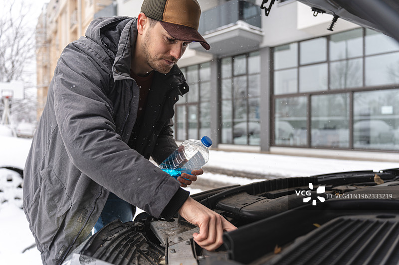 年轻白人男子打开储液罐倒入挡风玻璃清洗液图片素材