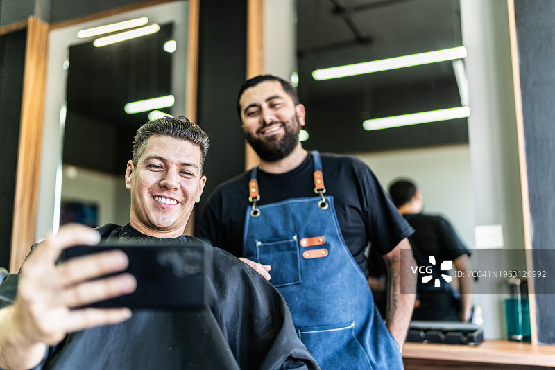 中年男人和理发师用手机录制社交媒体视频图片素材