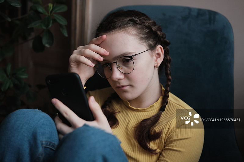 青少年与网络欺凌。少女在家中使用手机，悲伤的青少年看着手机屏幕图片素材