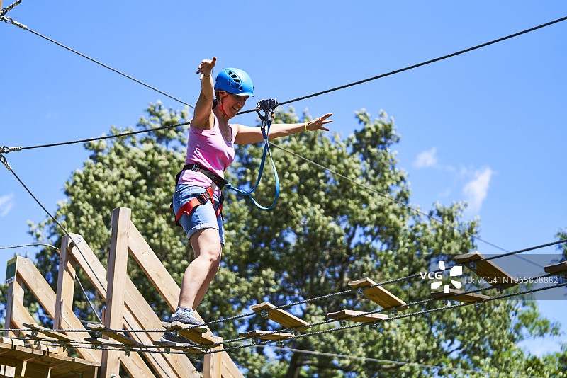 兴奋的女人带着安全设备过吊桥，背景是一棵绿树图片素材