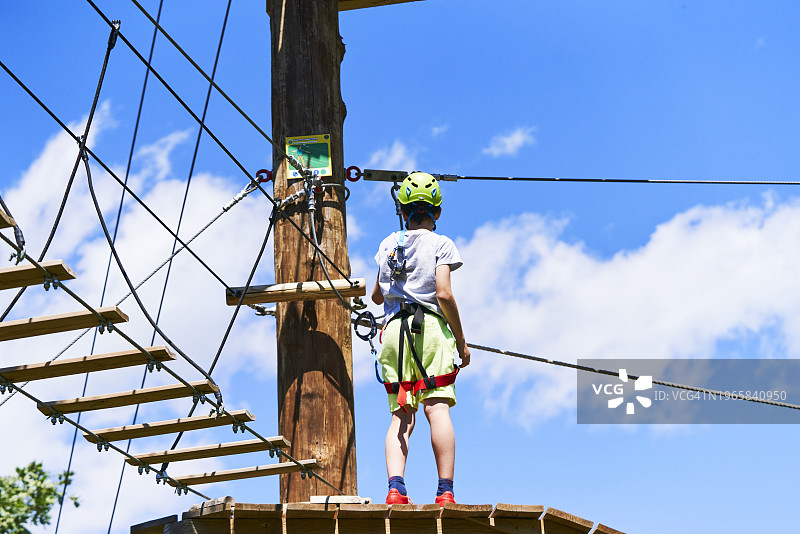 男孩站在木制平台上，背对着一面，背景是天空和吊桥图片素材