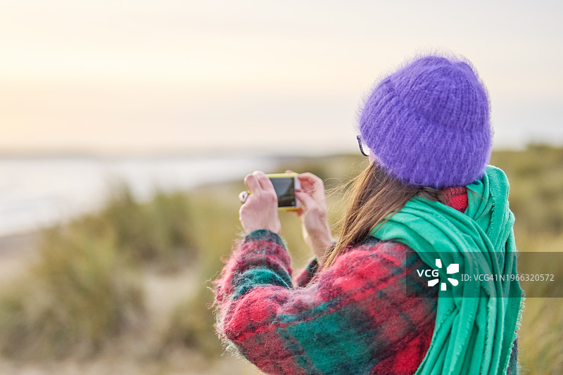 在冬天海滩上用手机拍照的女人图片素材