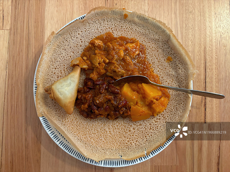 英吉拉面包上的埃塞俄比亚食物选择：牛肉萨摩萨、用贝贝雷香料、洋葱和大蒜腌制的鸡肉条；香料南瓜；芸豆图片素材