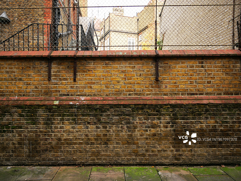 带有围栏的做旧砖墙，远处可见建筑物，脏污的人行道，阳光充足的伦敦图片素材