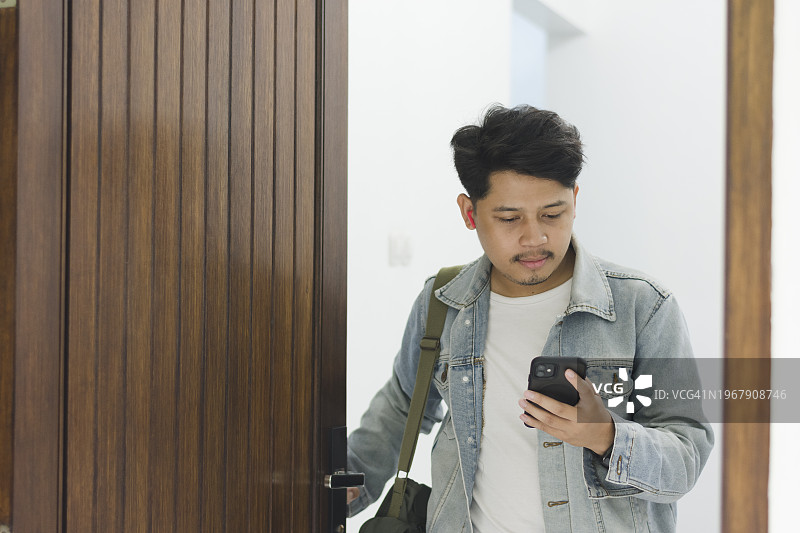 穿着牛仔外套的年轻亚洲男人戴着耳机离开家图片素材