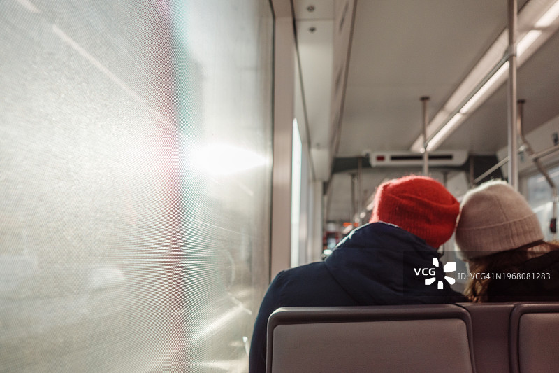 戴着帽子的情侣乘客并排坐在阳光下的背影图片素材