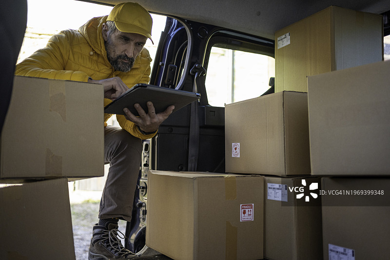 快递员用平板电脑检查要送的邮政包裹图片素材