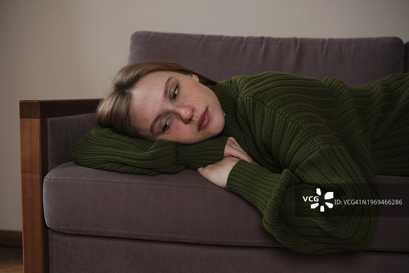 悲伤和沮丧。悲伤的千禧一代女孩躺在沙发上看着旁边，感到不安，沮丧的女人在家里，应对分手。心理健康概念图片素材